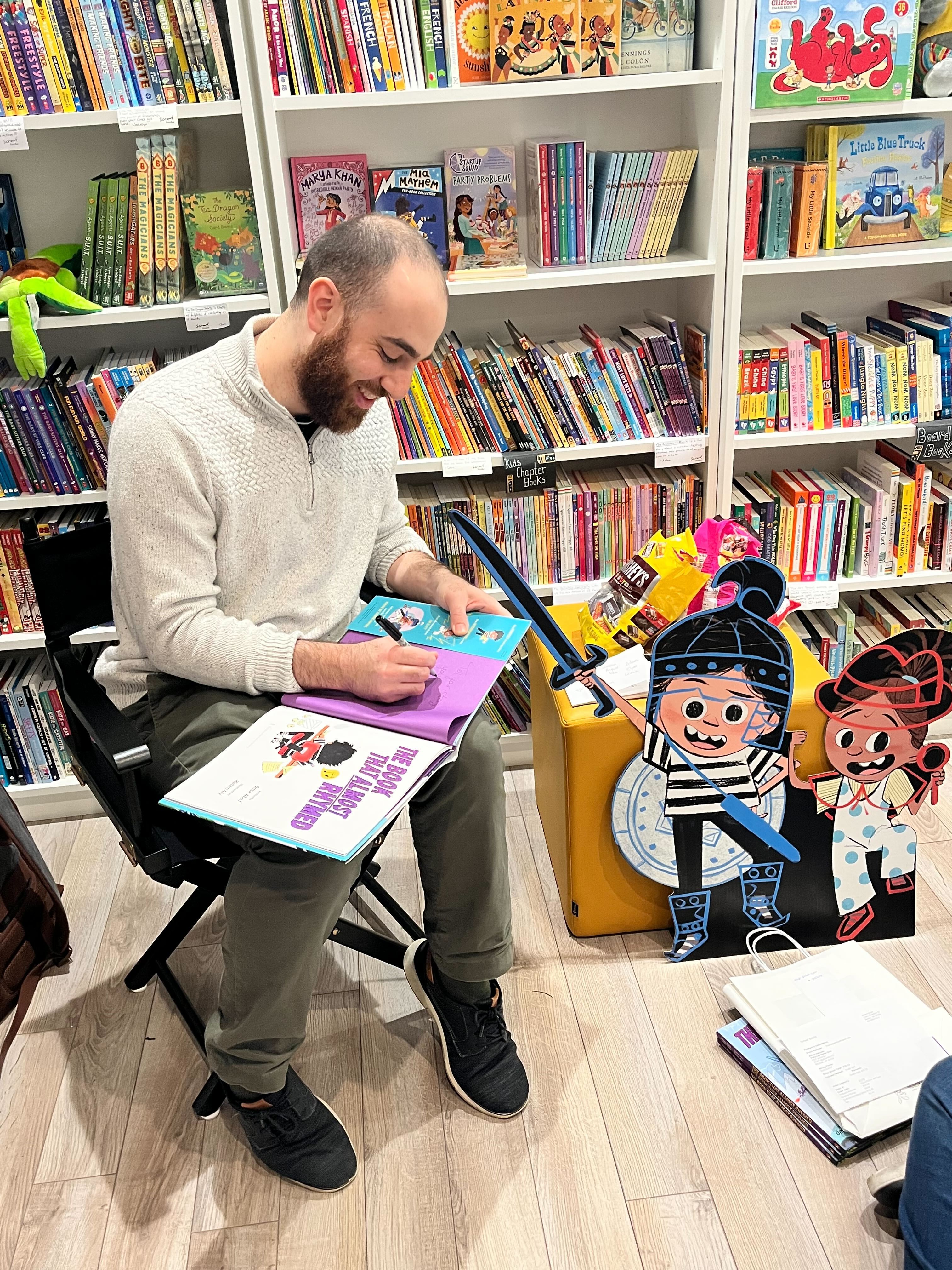 Omar signing a copy of The Book That Almost Rhymed beside a cardboard cutout of the characters