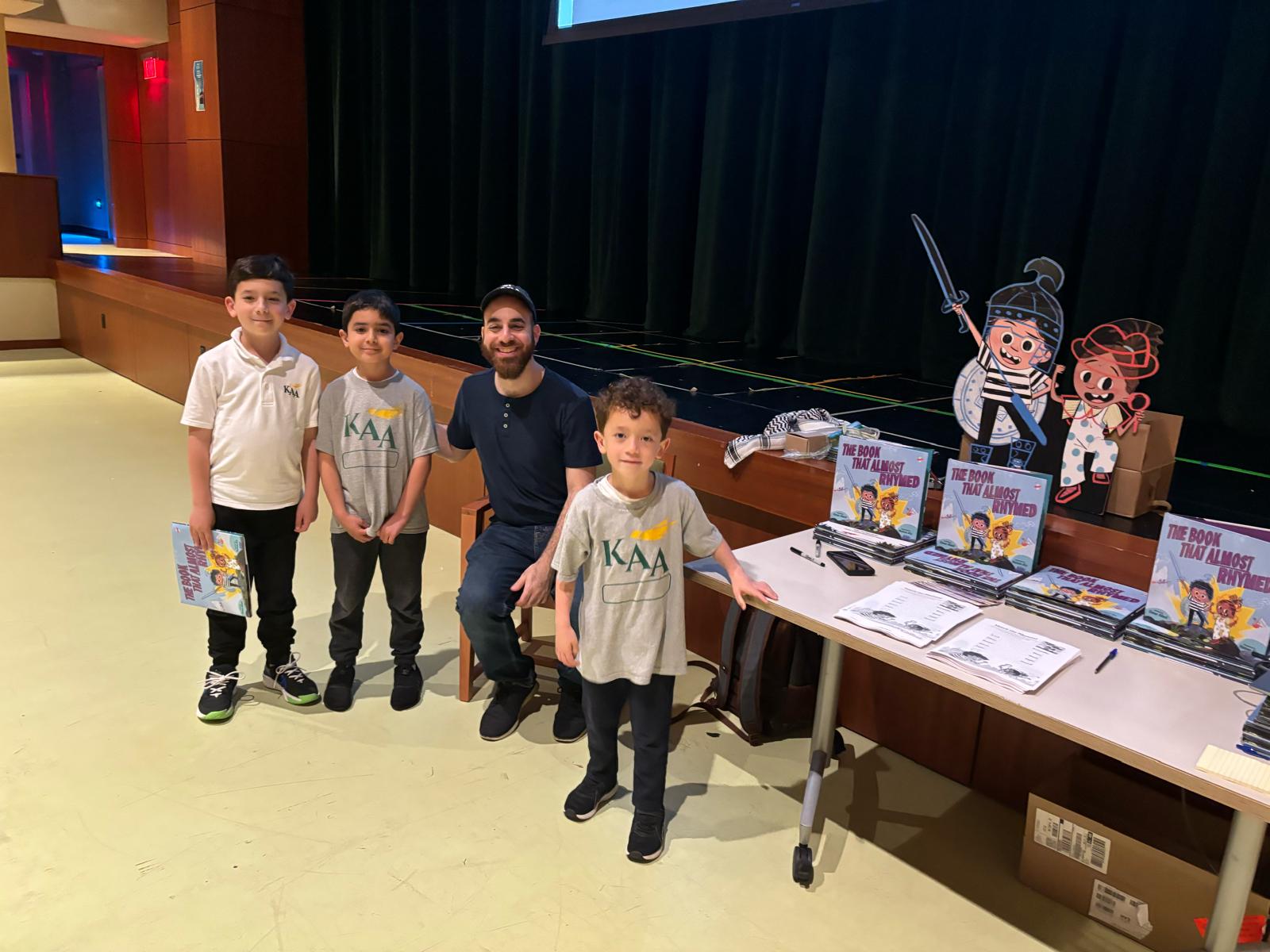 Omar posing with students by a display table for The Book That Almost Rhymed